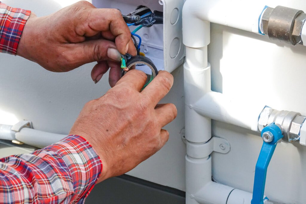 Technician repairing electrical wiring near an RV water pump system during maintenance